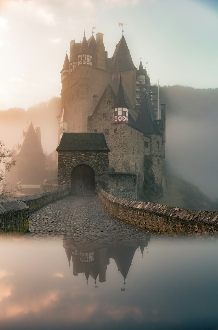Eltz Castle rising out of morning mist above a mirrored reflection